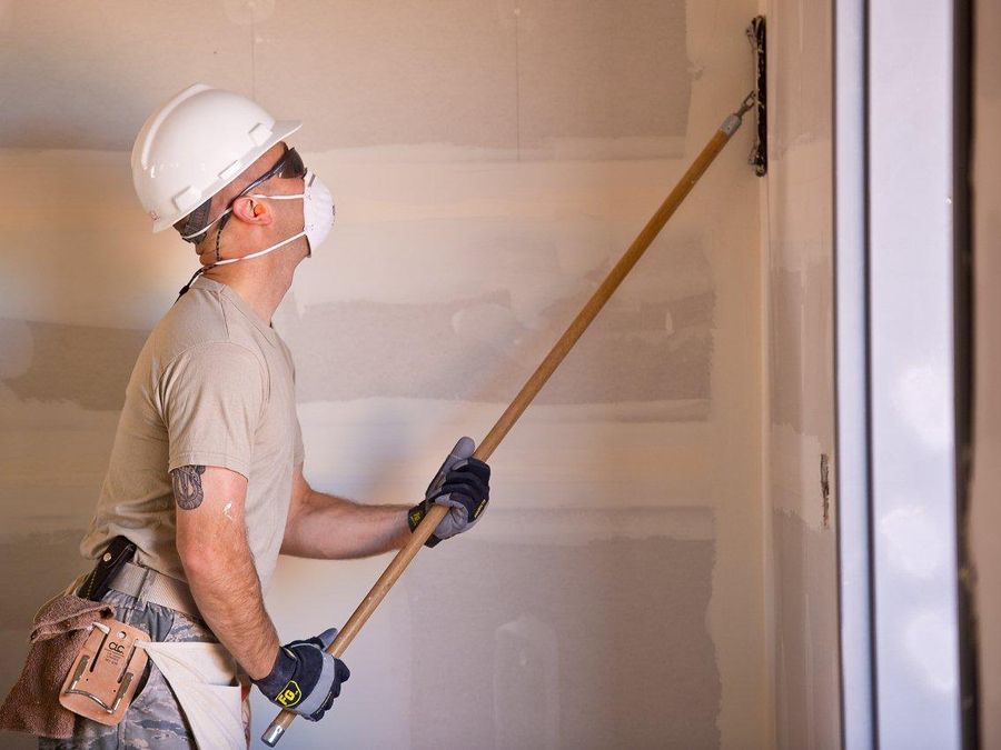 Finisher sanding a drywall wall with a pole sander